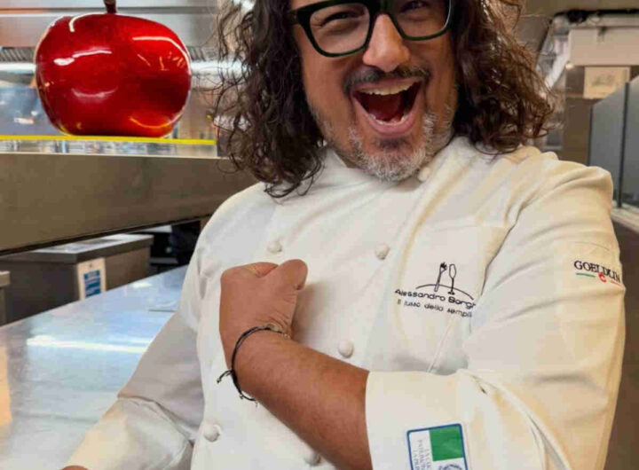 Alessandro Borghese nella cucina del suo ristorante che mostra orgoglioso lo scudetto della cucina italiana patrimonio dell'unesco