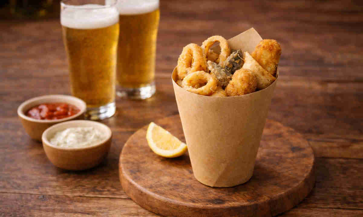 Cuoppo napoletano con fritti croccanti misti su tavolo di legno con accanto due birre chiare e delle salse per fritti