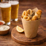 Cuoppo napoletano con fritti croccanti misti su tavolo di legno con accanto due birre chiare e delle salse per fritti