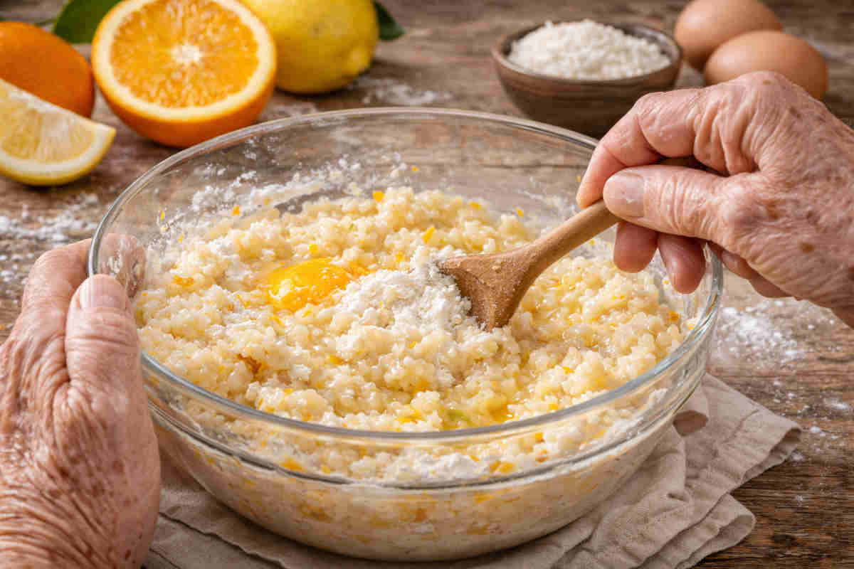 Mani di una signora anziana che mescola l'impasto per fare delle Frittelle di riso di San Giuseppe