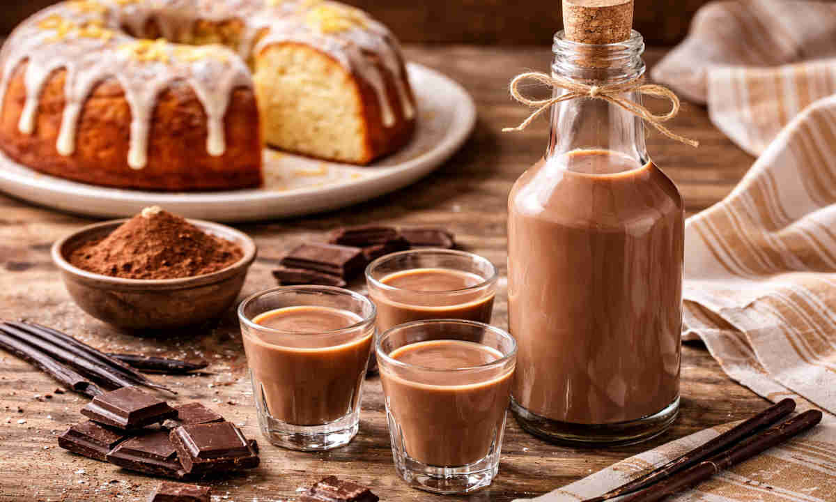 Liquore al cioccolato su tavolo di legno rustico con dietro un ciambellone alla vaniglia