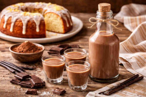 Liquore al cioccolato su tavolo di legno rustico con dietro un ciambellone alla vaniglia