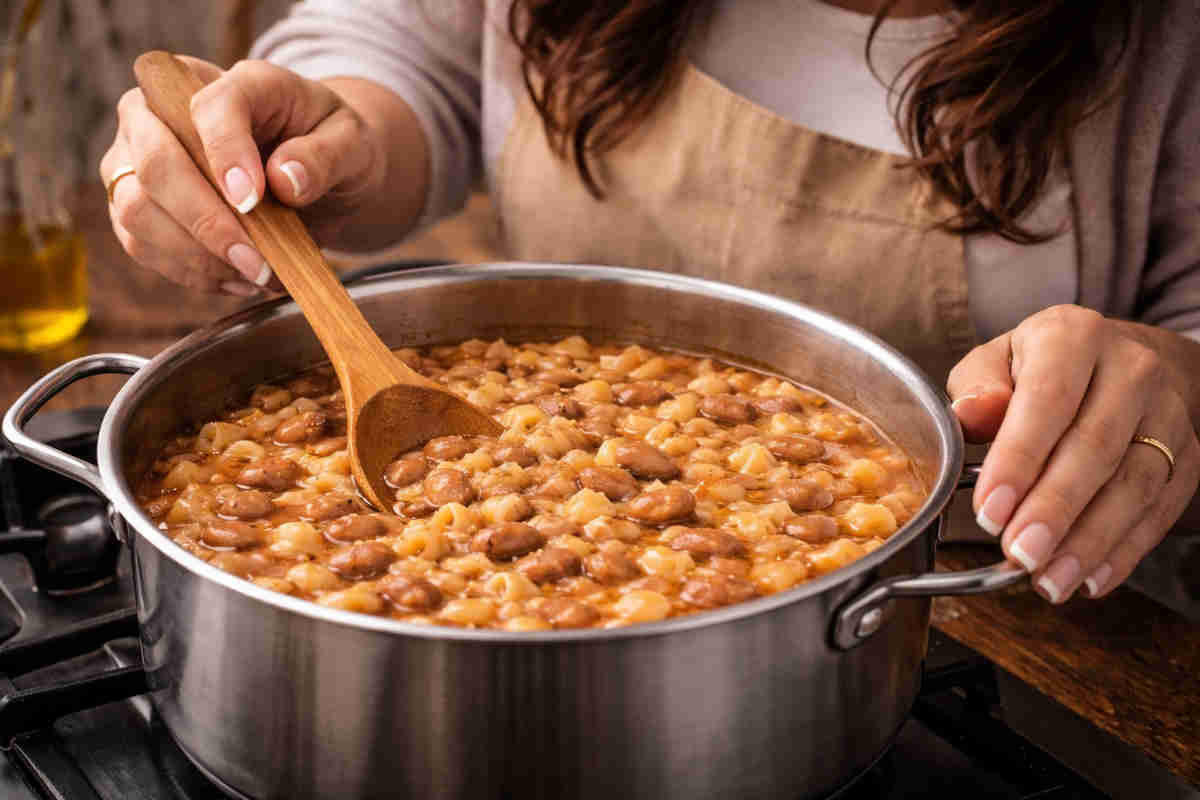 Donna con capelli castani ai fornelli mentre prepara una pasta e fagioli cremosa