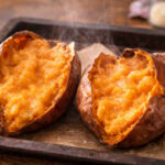 Teglia da forno con carta forno e sopra delle patate dolci cremose appena sfornate